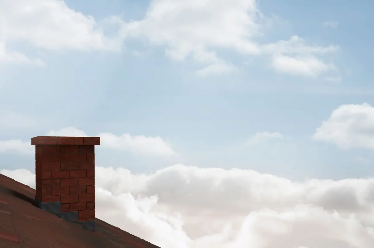 A brick chimney on a tiled roof against white clouds