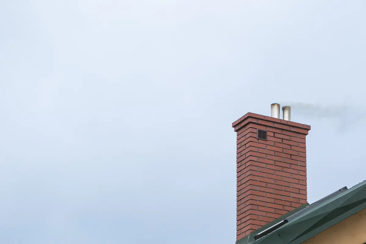 A brick chimney with a metal cap against a pale sky