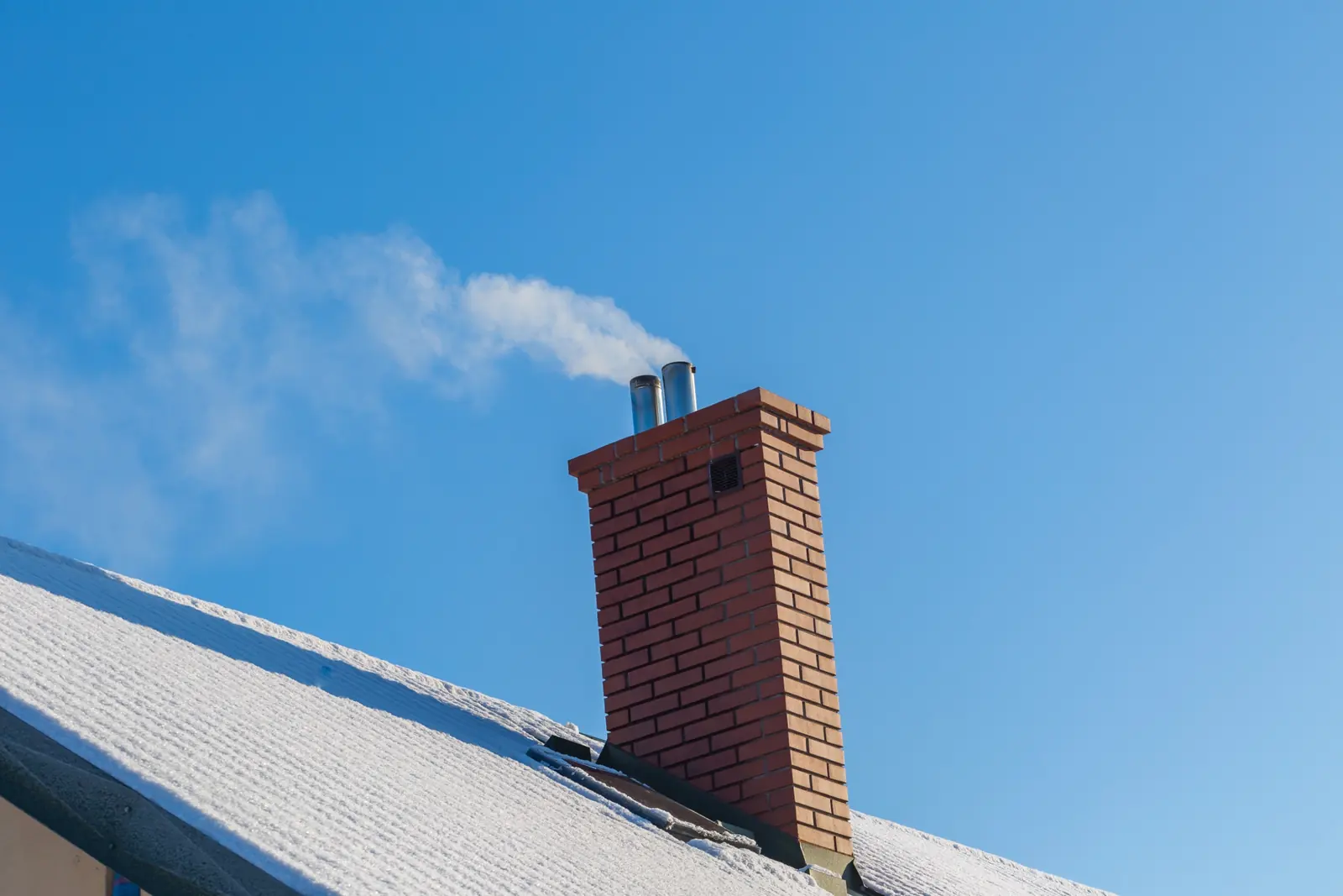 A brick chimney with smoke rising into a blue sky