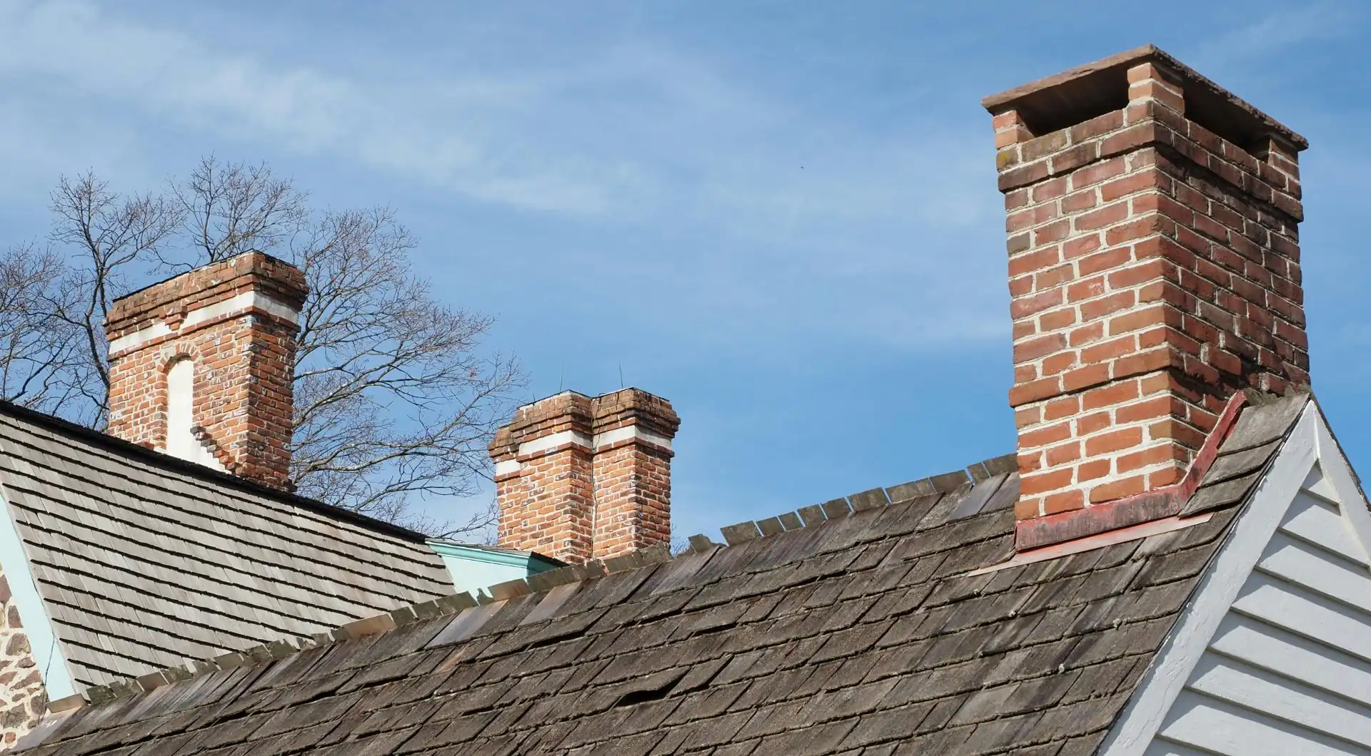 Brick chimneys on a roof against a blue sky with bare trees