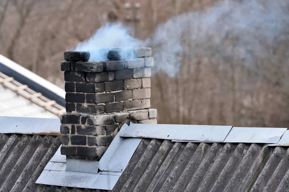 Smoke rising from a weathered masonry chimney on a metal roof