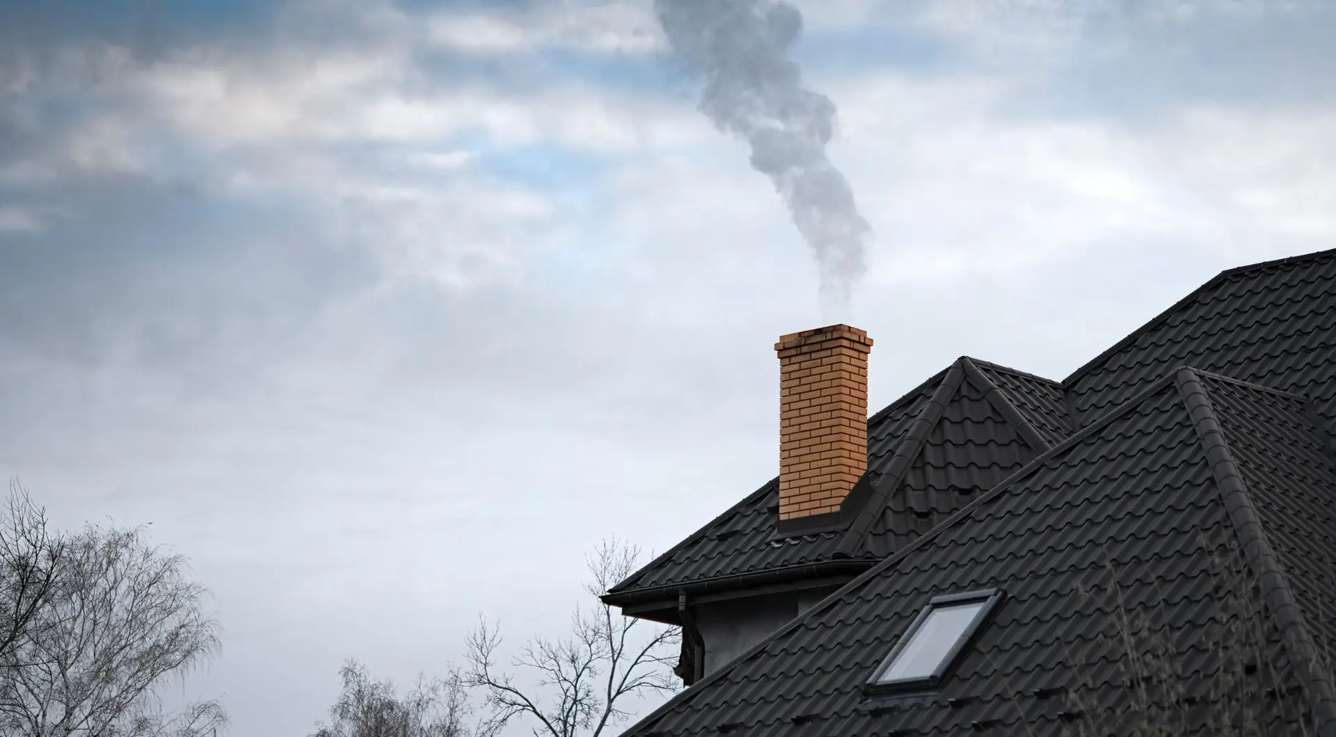 Smoke rising from a brick chimney on a dark shingle roof